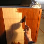 Applying wood stain to a cabinet with a brush, just before wiping off the stain with a rag.